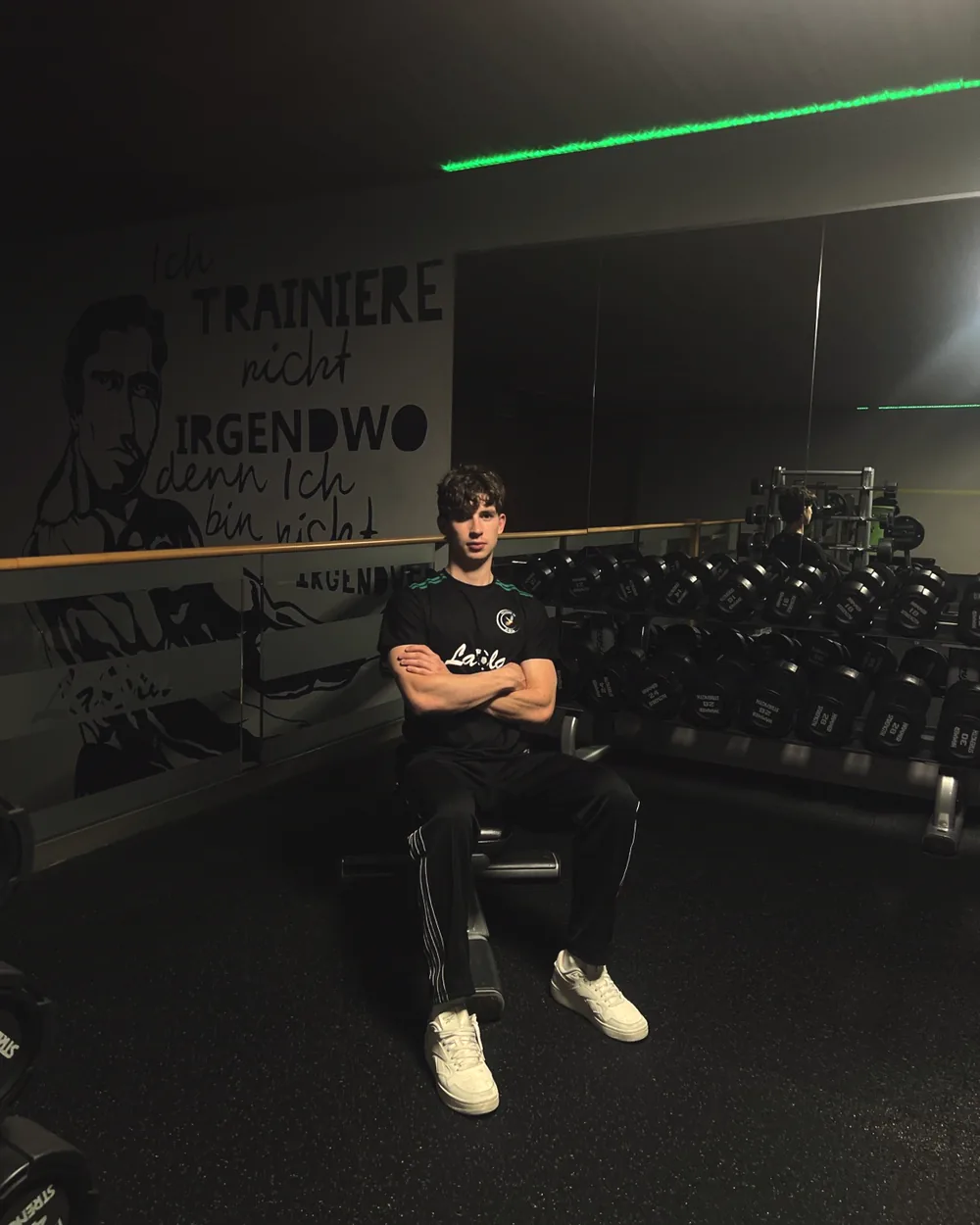 Daniel Wollenberg sitzt mit verschränkten Armen auf einer Hantelbank im Fitnessbereich des LaOla Centers